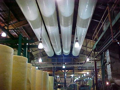 Four fabric air distribution ducts running along a plant ceiling above large rolls of material.